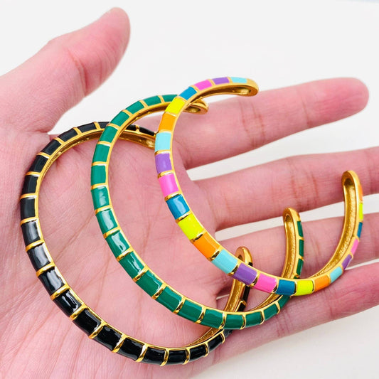 Colorful bangles on a hand with a white background. Open cuff bangle showing green enamel detail and gold platin