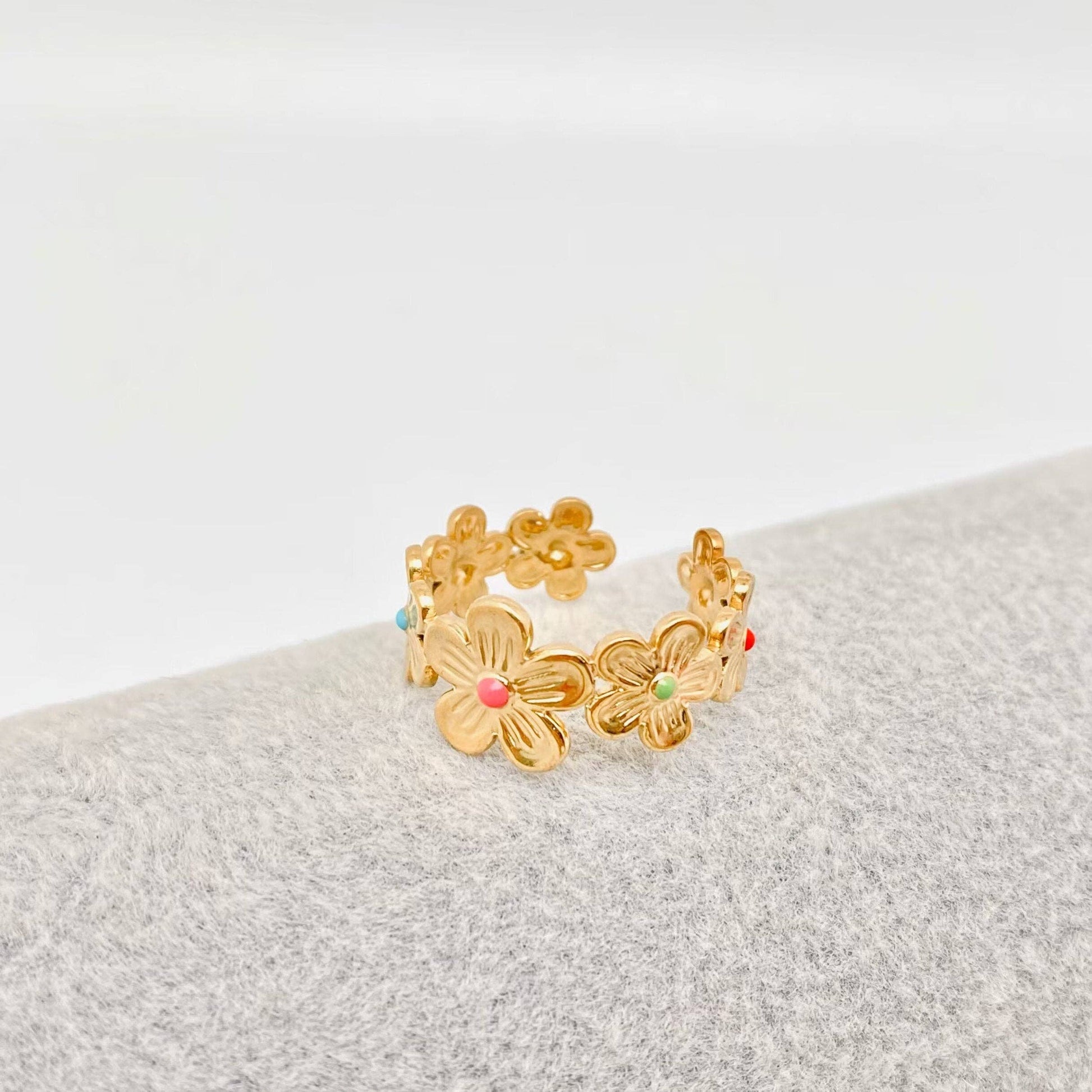 Gold floral ring with colorful enamel dots on a textured floral surface