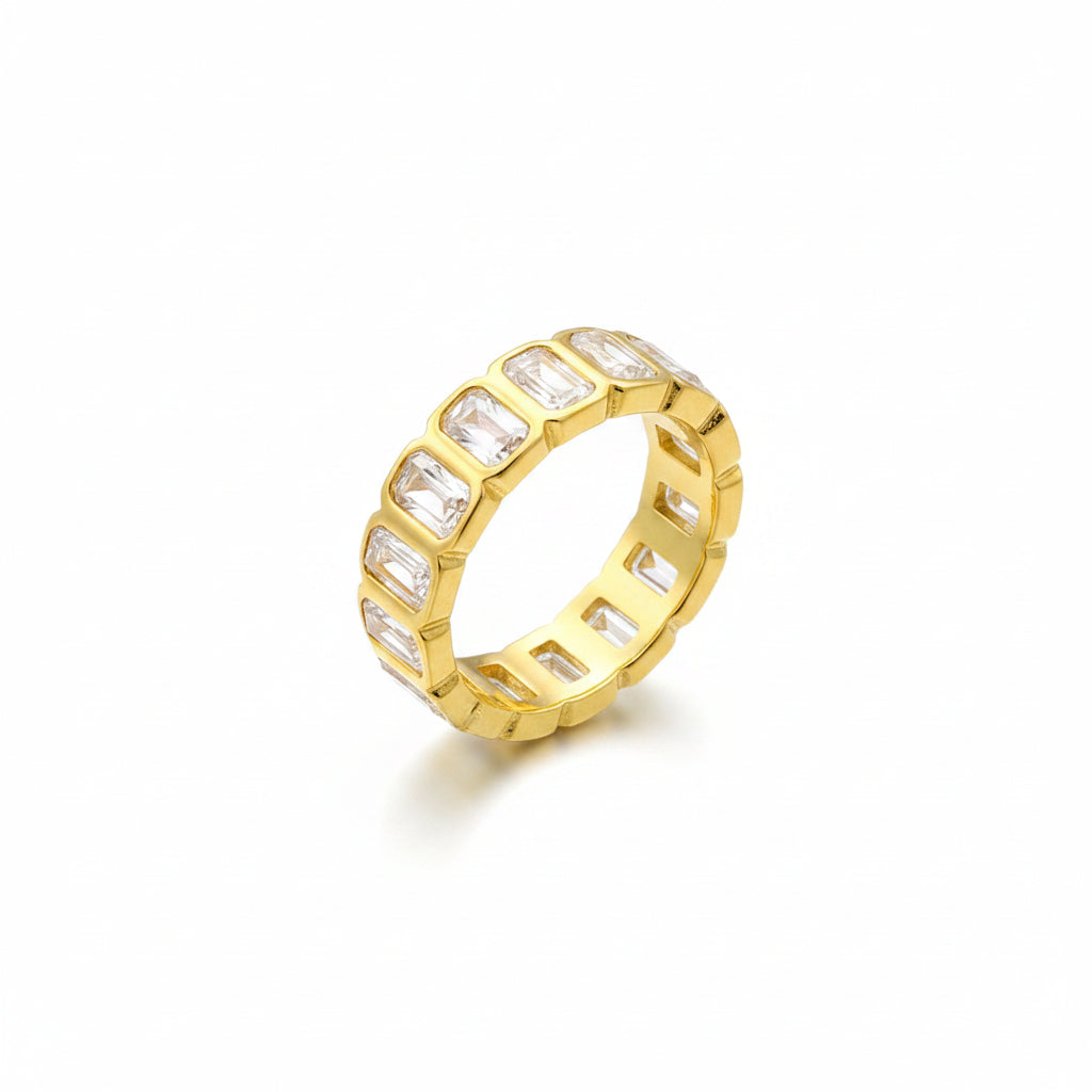 Gold ring with clear stones on a finger against a gray background