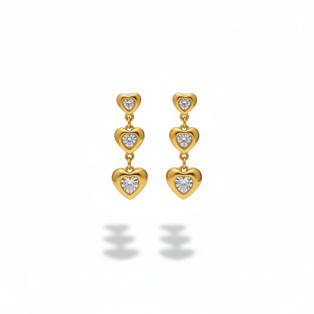 Gold heart-shaped earrings with clear stones on a gray stand.