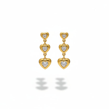 Gold heart-shaped earrings with clear stones on a gray stand.