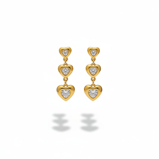 Gold heart-shaped earrings with clear stones on a gray stand.