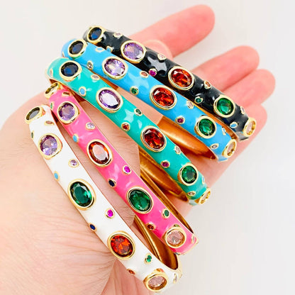 Colorful enamel bangles with gemstone-like embellishments on a hand against a white background