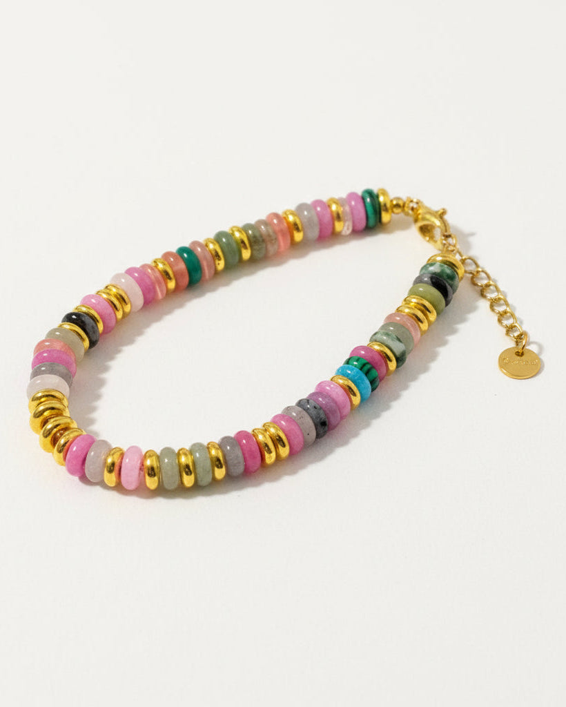 Colorful beaded bracelet with gold chain held in hand against a textured gray background