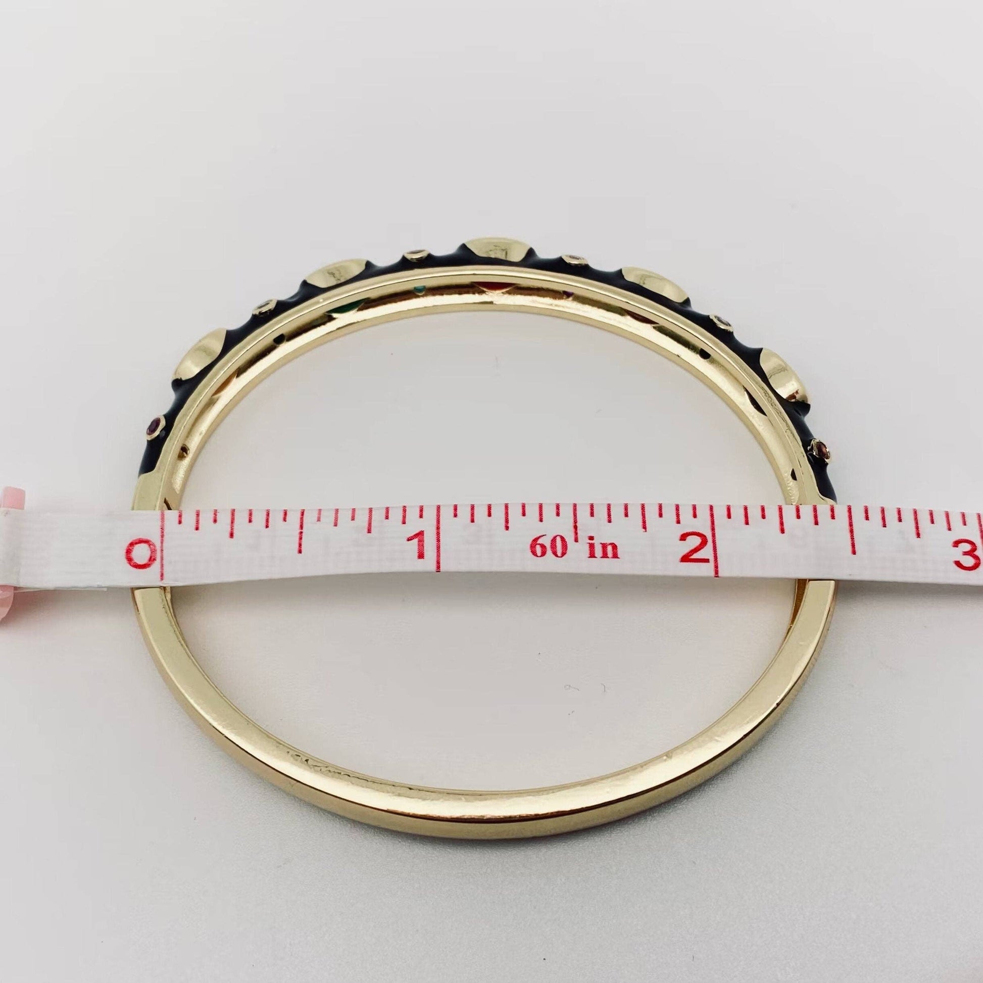 Gold bangle with measuring tape showing size on a white background