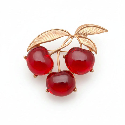 Brooch with red cherries and gold leaves on a gray background