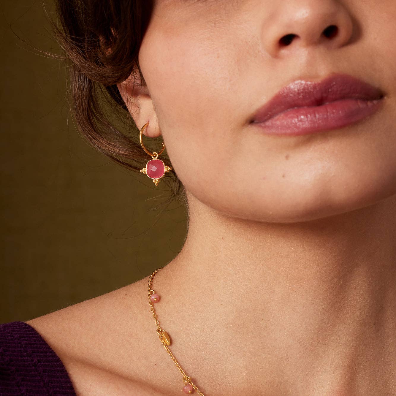 Close-up of a model wearing gold and pink gemstone earrings and a necklace