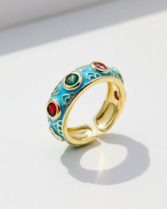 Gold ring with blue enamel and colored gemstones on a white background