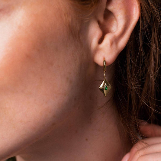 Gold huggie earring with a green gemstone worn by a person