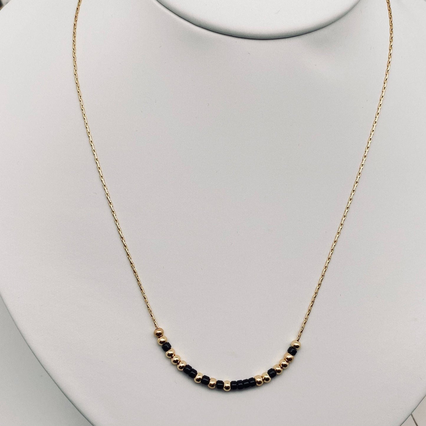Necklace with black beads on a mannequin neck against a light gray background