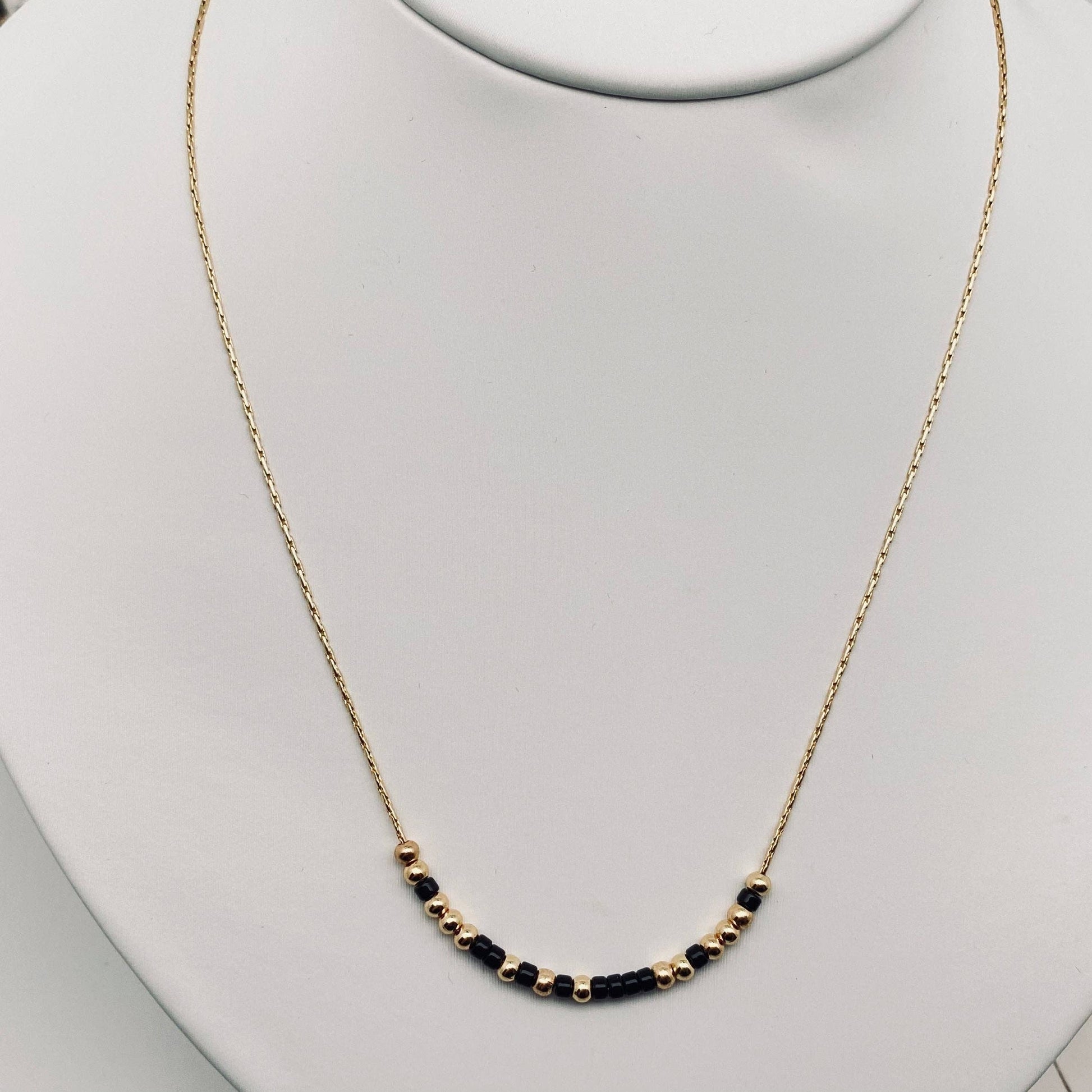 Necklace with black beads on a mannequin neck against a light gray background