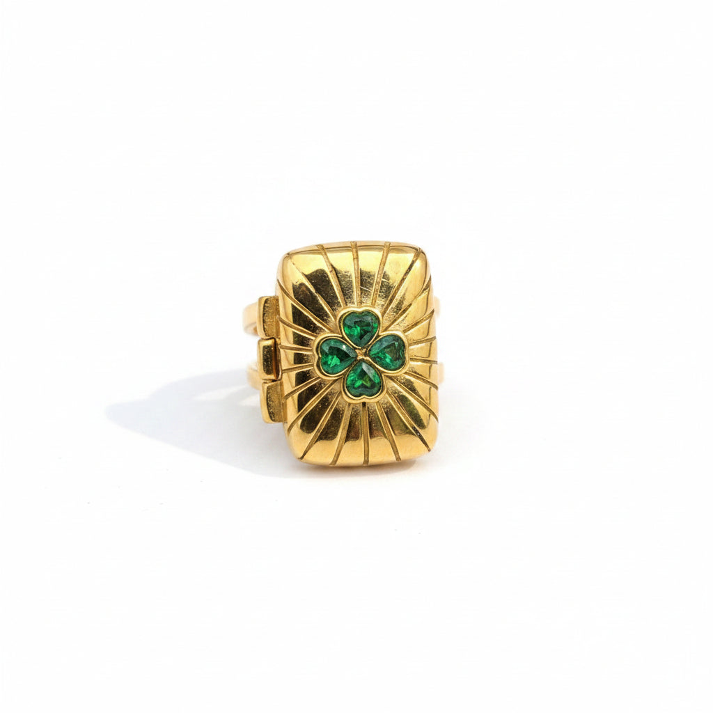 Gold ring with green gemstones held on a hand against a dark background