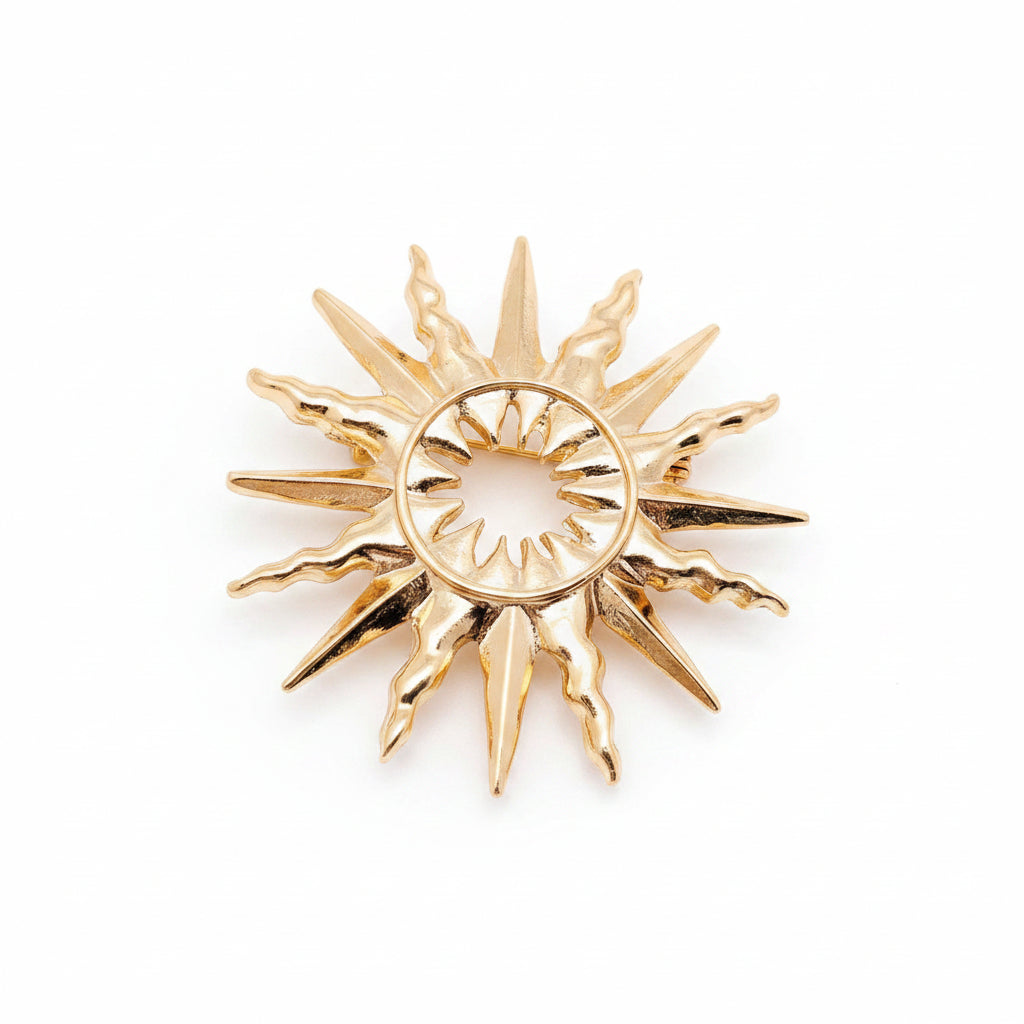 A gold-toned sunburst pendant or brooch with a circular center and radiating pointed rays, against a light neutral background.