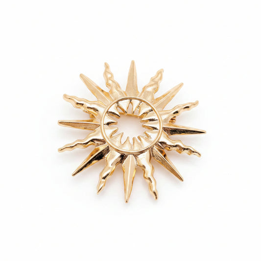 A gold-toned sunburst pendant or brooch with a circular center and radiating pointed rays, against a light neutral background.