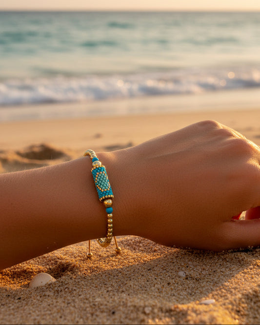 Beaded bracelet with gold and turquoise beads on a sunkist arm on the beach