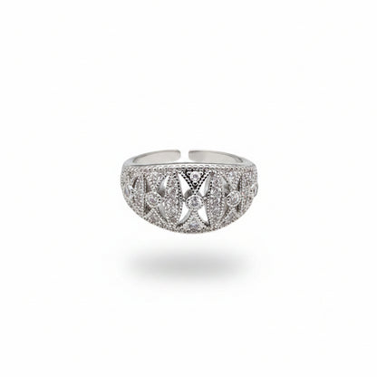 A silver-toned filigree ring with clear stones, shown resting on a person's fingers against a dark gray background.