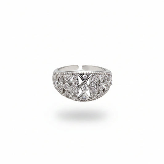 A silver-toned filigree ring with clear stones, shown resting on a person's fingers against a dark gray background.